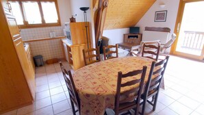 A cozy kitchen with wooden cabinets, a tiled floor, a round table with chairs, and a window providing natural light. - LA GRANGE - 2 VAST CHALET APARTMENTS (70m2) - ALPE D'HUEZ ACCESS (Vaujany)