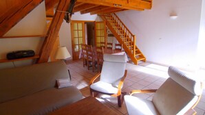 A loft-style room with a wooden staircase, a sofa, two armchairs, and a dining table. - LA GRANGE - 2 VAST CHALET APARTMENTS (70m2) - ALPE D'HUEZ ACCESS (Vaujany)