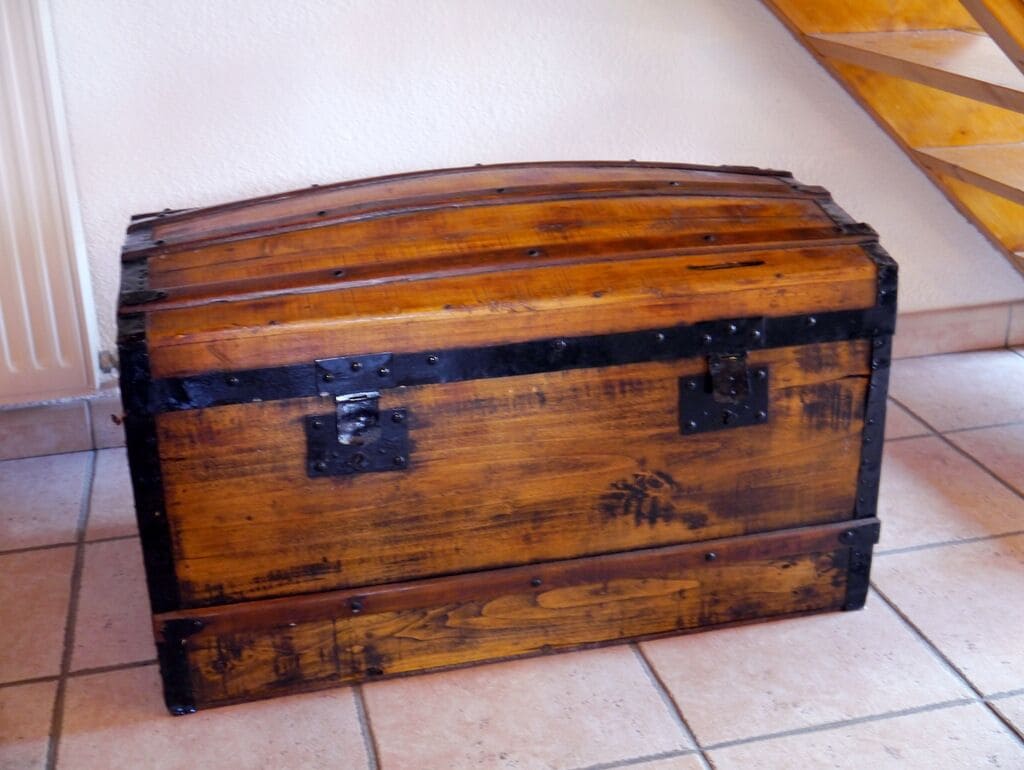A wooden chest with metal reinforcements, placed on a tiled floor near a staircase.
