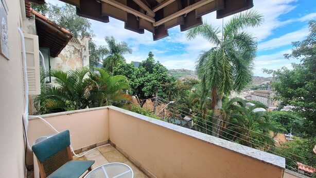 A balcony with a view of a cityscape, surrounded by greenery and palm trees.