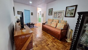 A living room with a sofa, wooden flooring, a TV, and framed pictures on the wall.