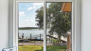 Vista a través de una ventana de un lago con barcos, un muelle y una zona cubierta de césped.