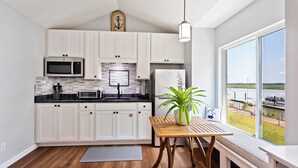 Una cocina moderna con armarios blancos, un microondas, un refrigerador y vistas a un puerto deportivo a través de amplias ventanas.
