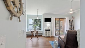 Una sala de estar con suelo de madera, un sofá de cuero marrón, un televisor montado y una ventana con vista a una terraza.