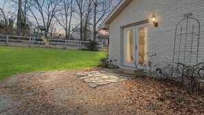 Ein Haus mit einem steinbelagten Weg, der zu einer weißen Tür führt, einem eingezäunten Hof und bodenbedeckenden Laub.