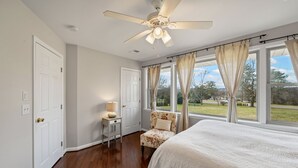 Ein Schlafzimmer mit einem großen Bett, einem Deckenventilator, einem Stuhl und einem Fenster mit Vorhängen.