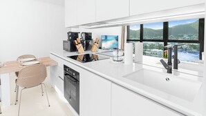 Een moderne keuken met een groot eiland, een eethoek met een houten tafel en stoelen, en uitzicht op een bergachtig landschap door grote ramen.