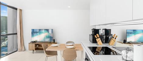 A modern kitchen with two TVs, a dining area with a wooden table and chairs, and a large window with a city view.