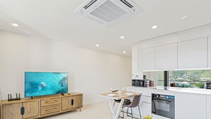 Eine moderne Küche mit weißen Schränken, einem Holztisch und einem Fernseher, der eine Szene mit Schwimmenden zeigt.