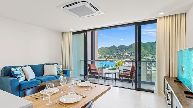 Ein modernes Wohnzimmer mit Essbereich, einer Couch und einem Balkon mit Blick auf eine Küstenstadt und Berge.