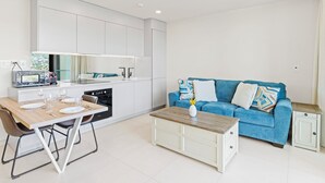 Eine moderne Küche mit weißen Schränken, einem Esstisch mit Stühlen, einem blauen Sofa und einem Couchtisch.