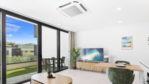 A modern living room with a large TV, a dining area, and a balcony with a view of the city. - B204 - Amazing 1 Bedroom with terrace (Sint Maarten)