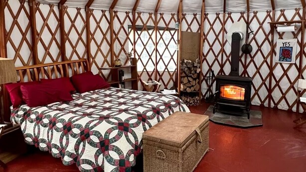 A yurt interior with a bed, a bench, a fireplace, and a lattice wall. - Yurt in Middlebury, Vermont (Middlebury)