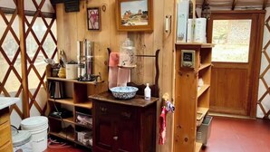 A rustic wooden interior with a wooden cabinet, shelves, and a framed picture. - Yurt in Middlebury, Vermont (Middlebury)