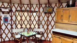 A tented room with a glass table and chairs, a wooden cabinet, and a sign indicating 'Dancing Gardens'. - Yurt in Middlebury, Vermont (Middlebury)