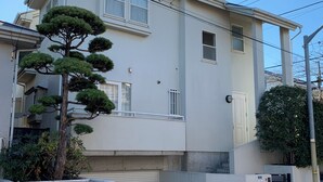 A two-story residential building with a garage, a small balcony, and a tree in front. - Large 3-bedroom house in Ota-ku suburb with garden. Close to city and airport. (Ota City)