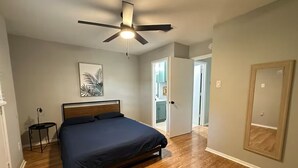 Une chambre à coucher avec un lit, un ventilateur de plafond, un tableau encadré au mur et un plancher en bois.