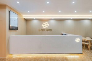 En receptionsdisk med et U-free hotel logo, et fladskærms-tv og et træbord til højre.