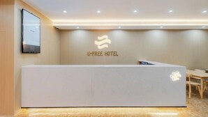 Un mostrador de recepción con el logo de hotel U-free, una pantalla digital y una zona de estar con mesas.