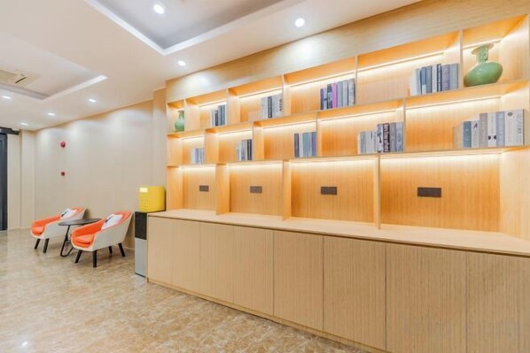 Un espace d’accueil avec un comptoir en bois, des étagères et deux chaises orange.
