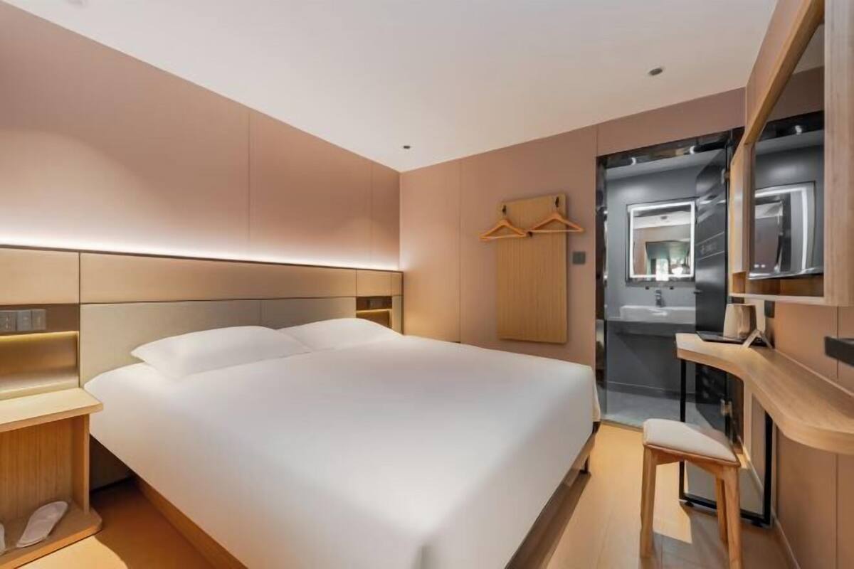 Una habitación de hotel moderna con una cama grande, mesitas de noche, un espejo y una pequeña zona de estar.