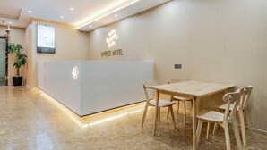 Zona de recepción de un hotel con diseño moderno, que incluye un mostrador de recepción, un área de descanso con sillas de madera y una planta en maceta.