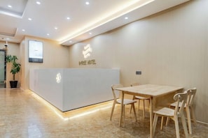 Un comptoir d’accueil avec un logo, une table en bois et des chaises dans le hall d’un hôtel.