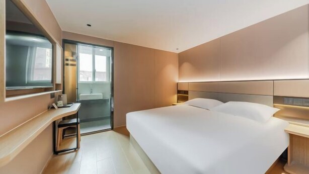 Una habitación de hotel moderna con una cama grande, un escritorio y un baño visible a través de una puerta de cristal.