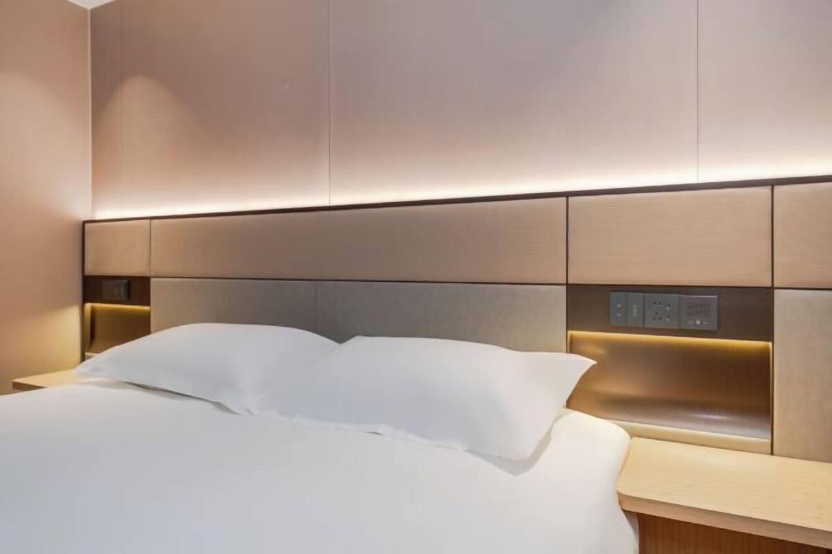 Una habitación de hotel moderna con una cama grande, una mesita de noche y un panel de control en la pared.
