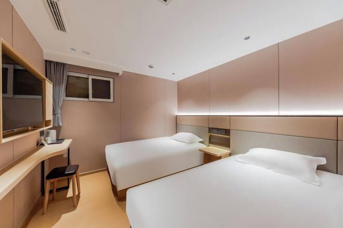 Habitación de hotel con dos camas, un escritorio, una silla y un televisor.