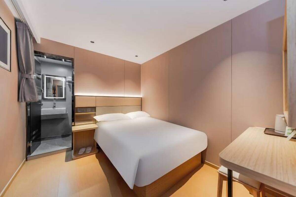 Una habitación de hotel moderna con cama, mesita de noche y un pequeño escritorio con silla.