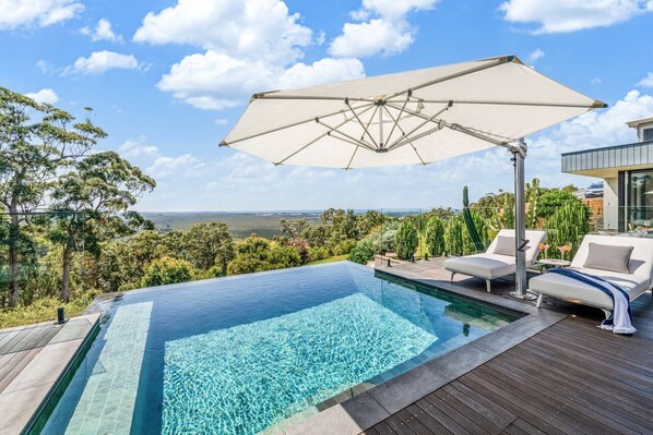An infinity pool with a clear view of the landscape, a wooden deck, and a lounge area with a canopy.