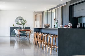 Une cuisine moderne avec un coin bar, une table à manger avec des chaises et un grand miroir.