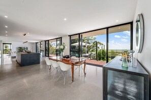 Une cuisine moderne dotée d’un îlot central, d’un coin repas avec une table en bois et des chaises blanches, et de grandes portes-fenêtres coulissantes donnant sur une terrasse extérieure.