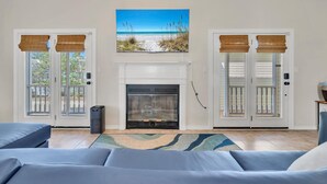 A living room with a fireplace, a large window with blinds, and a blue sofa. - Charming Destin Home | Yard, Pool & Beach Access (Destin)