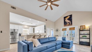 A spacious living room with a blue sectional sofa, a patterned rug, and a ceiling fan. - Charming Destin Home | Yard, Pool & Beach Access (Destin)