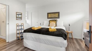 A bedroom with a bed, a wooden ladder, a small table with a lamp, and a framed picture on the wall.
