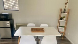 A dining area with a white table, four white chairs, a wooden tray, a black refrigerator, a white radiator, and a wooden shelf with a plant.
