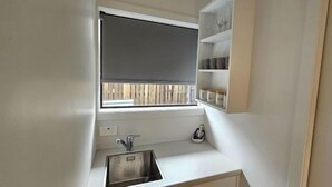 A compact kitchen with a window, a sink, and shelves above the counter.
