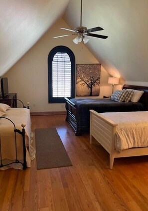 A bedroom with two beds, a ceiling fan, a window with blinds, and a painting on the wall.