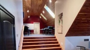 Un escalier en bois mène à un niveau supérieur où se trouvent un mur rouge et un piano.