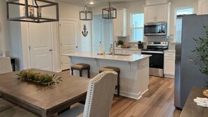 Una cocina moderna con una isla central, muebles blancos, electrodomésticos de acero inoxidable e iluminación colgante.