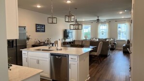 Una cocina moderna con armarios blancos, lavavajillas e isla central. Hay una zona de comedor con sofá y sillas.