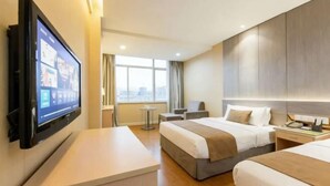 Ett hotellrum med två sängar, en tv som är monterad på väggen, ett litet bord och ett fönster med gardiner.