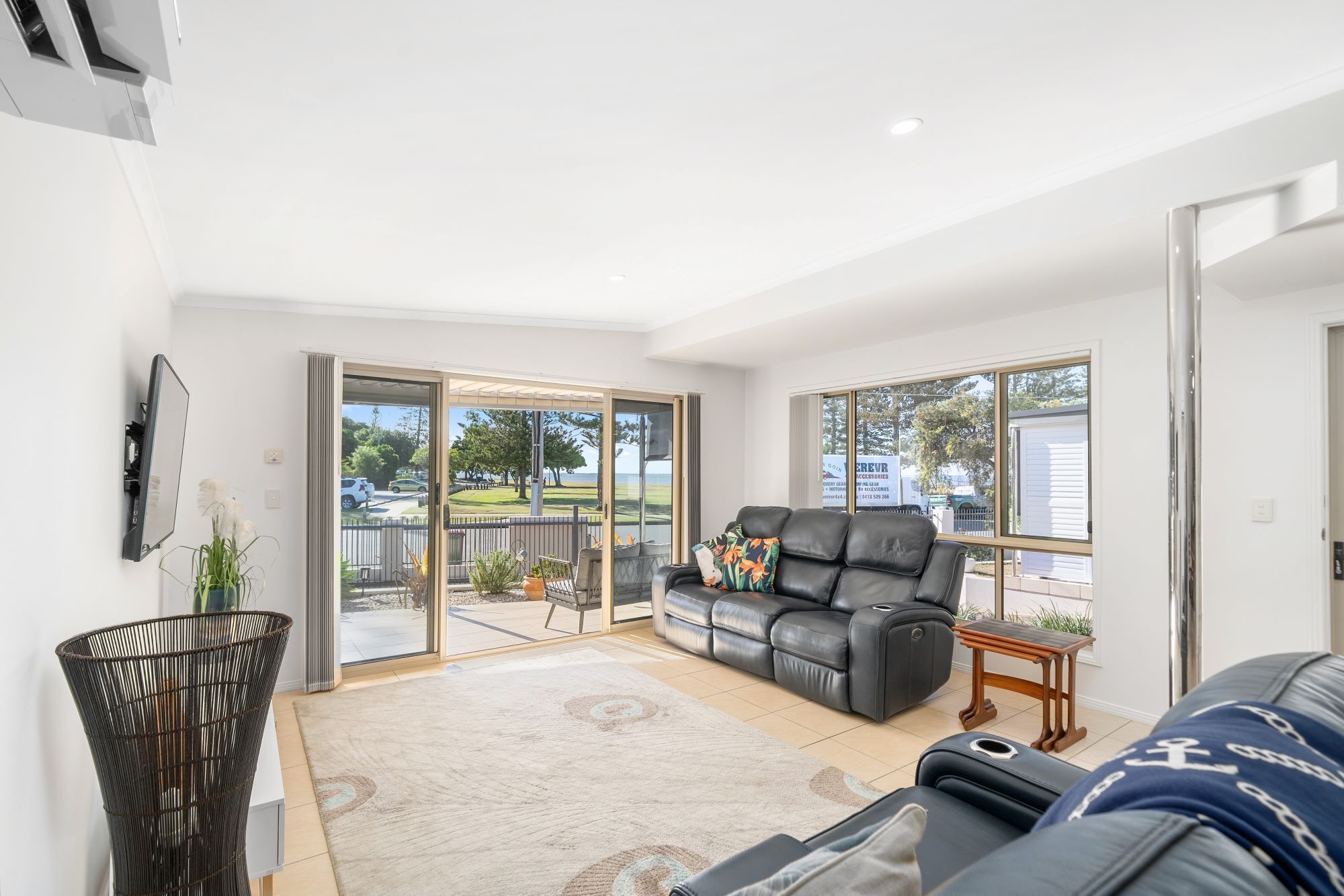 A spacious living room with a black leather sofa, a patterned rug, and a view of the outdoors through large sliding glass doors.