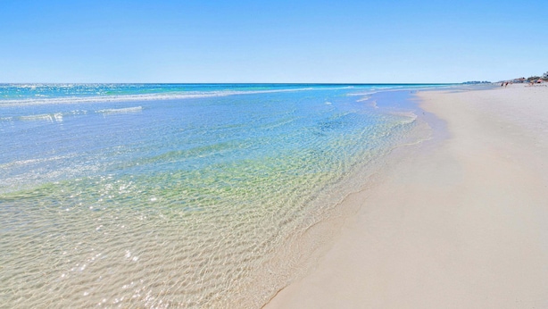 A beach with clear shallow waters and a wide sandy shore.