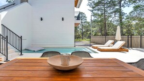 A wooden table with a bowl and a cup, a pool, lounge chairs, and a staircase leading to a white building.