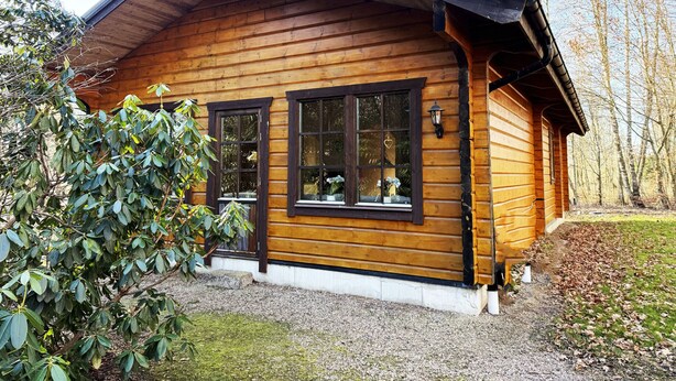 Une cabane en bois avec un toit en pente, de grandes fenêtres et des fondations en pierre.