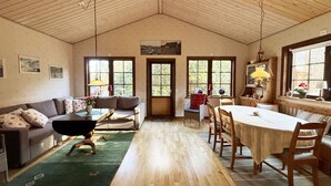 Une pièce spacieuse avec un plafond haut, un plancher en bois, un ensemble de canapés, une table à manger avec des chaises et de grandes fenêtres qui laissent entrer la lumière naturelle.