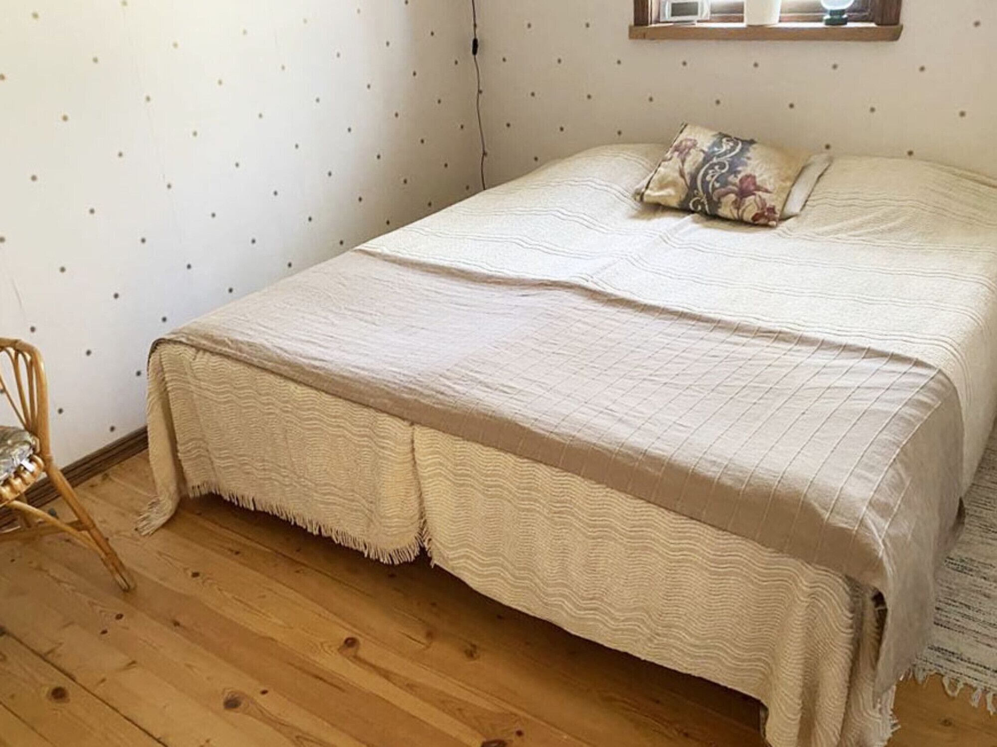 Ett sovrum med en säng, ett trägolv, en stol och en vägg med ett prickigt mönster.
